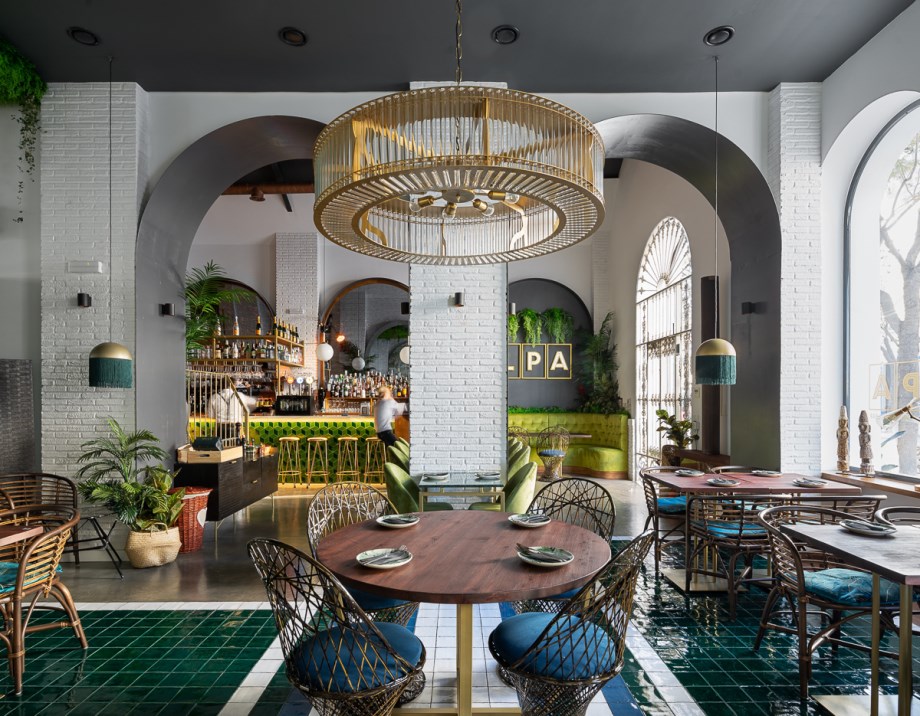 LPA, el nuevo restaurante de moda en Ayamonte, un proyecto de CM4. Con una gran parte de la cliente extranjera y siendo LPA uno de los referentes del municipio de Ayamonte (ciudad costera de la provincia de Huelva), el nuevo diseño e interiorismo de la reforma del local pretende sumergir al usuario en una experiencia fresca y acogedora, que realce los valores del clima mediterráneo.El primer obstáculo consistió en unir dos naves industriales y recuperar su estado y aspectos originales para después crear un espacio alegre y exótico, en el que la luz natural se derrama por todo el restaurante, y en la que los colores vivos y el blanco sirven de telón de fondo para una experiencia gastronómica inigualable.El local presenta dos zonas bien distinguidas, dos mundos. En el derecho nos encontramos con la zona de barra y coctelería, más informal, mientras que en la nave izquierda tenemos el comedor más grande. La cocina por otro lado, atraviesa las dos naves en la parte trasera, por lo que permite el paso de personal a las dos zonas de manera independiente.El ladrillo taco original de los muros, se pinta de blanco junto con el resto de paramentos para potenciar las grandes cristaleras y la luz natural tan presente en la costa. Con esto como base, se elige un mobiliario alegre, con tonos verdes claros y azules, que también podemos observar en el suelo de barro esmaltado. A esto se le suman un reservado decorado en tonos dorados y un salón superior desde el que se puede ver toda la altura de las naves y el sistema estructural de cerchas.Mármoles blancos y verdes, maderas, y vinilos en tonos claros completan los materiales bases del diseño.El objetivo y resultado final lleva al usuario a disfrutar de la comida como si al aire libre se tratase y acompañado siempre de un entorno mediterráneo.